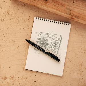 Lucky Jack 9-in-1 Builder’s Pen multi-tool resting on a notepad with a hand-drawn design sketch, emphasizing its role as an everyday carry writing and utility tool.