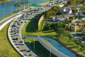 Aerial view of a highway with a sound attenuation wall separating traffic lanes from nearby residential neighborhoods.