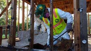 A TXCC program participant wearing a hazmat suit and PPE uses tools to clear damage from a residential property during on-site disaster response.
