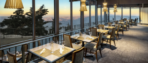 Elegant restaurant interior with panoramic windows, offering stunning mountain views at sunset. Cozy tables set for dining.