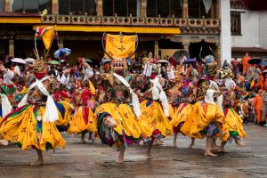 Colorfully dressed Bhutanese monks perform a traditional masked dance during a Tsechu festival at a monastery courtyard, celebrating spiritual heritage through rhythm, ritual, and vibrant costume.