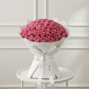 A large bouquet of vibrant pink roses is elegantly arranged in white wrapping and tied with a ribbon, placed on a round table. The setting feels luxurious and romantic.