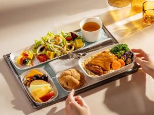 A Premium Economy Class meal served on China Airlines’ new white porcelain tableware, featuring a main dish of roast chicken with curry, rice, and vegetables, along with salad, bread, fruit, and tea, arranged neatly on a tray in warm natural light.