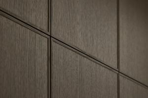 Extreme close-up of dark brown oak cabinetry showing the deep vertical wood grain and the thin, precise horizontal and vertical grooves of the handleless design.