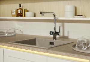 A modern kitchen sink area featuring a beige-toned composite sink, a sleek chrome faucet with a blue LED ring, and a light wood backsplash.