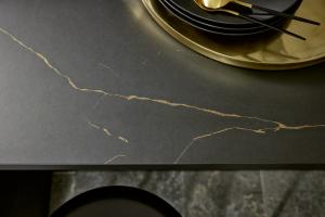 A close-up of a matte black countertop or splashback featuring a single, dramatic metallic gold-colored vein running diagonally across the surface.