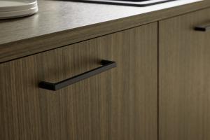 A close-up shot of two walnut-textured cabinet doors with a slim, horizontal matte black handle mounted on one side.