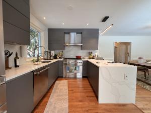 A contemporary U-shaped kitchen in Bethesda, MD, featuring dark grey flat-panel cabinets from the Manhattan Uni series. A large white quartz island with a waterfall edge and bold grey veining dominates the foreground. Stainless steel appliances, including