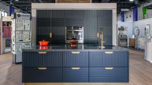 A high-end kitchen display in the Savona Green Brook showroom featuring black ribbed custom cabinetry, a dark waterfall island with a gold faucet, and integrated appliances.