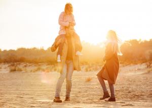 A parent carries a young child on their shoulders while another family member walks beside them outdoors at sunset, symbolizing family connection and well-being.