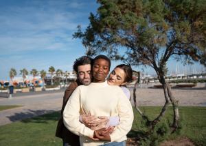 Three adults stand outdoors embracing one another, conveying emotional support, connection, and mental wellness.