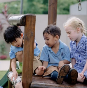Three pupils at The Independent School of Jakarta playing on a wooden play structure in a leafy school campus