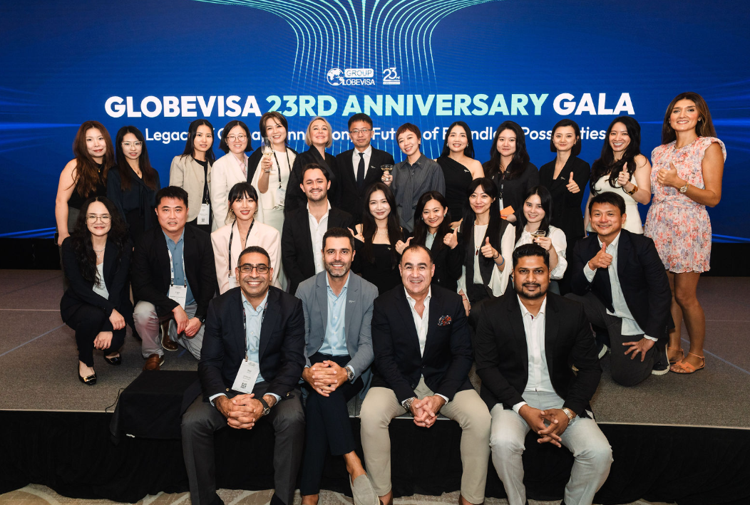 Group photo of Globevisa team members and partners at the 23rd Anniversary Gala in Singapore, standing in front of a blue backdrop celebrating the company's history.