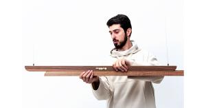 Designer holding the Moono sliding pendant light by SHRE Studio, showing its wooden modular structure.