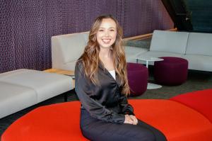 Rachel Sweet, a Kansas City University anesthesiologist assistant student, sits smiling on a red bench inside a modern campus lounge.