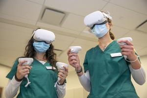 Two students in nursing scrubs wear VR headsets as part of a training exercise.