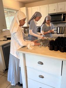 three sisters in the medicine making kitchen, standing at the counter, packaging salve