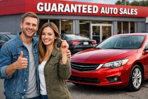 Happy couple holding car keys next to a red used car at Guaranteed Auto Sales in Johnston, Rhode Island