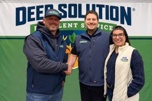 Co-founders Kris and Jaime Goodrich standing with newest franchisee, Tim Pollock, in front of a Deer Solution banner, marking a partnership with a handshake.