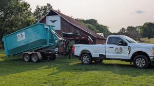 White Trash Pandy truck delivering a teal roll-off dumpster at a rural property with a barn in Middle Tennessee