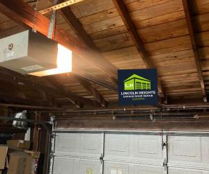 An overhead garage door opener motor with an illuminated light bulb mounted to a wooden ceiling beam, showcasing a professional installation by Lincoln Heights Garage Door Repair Experts.