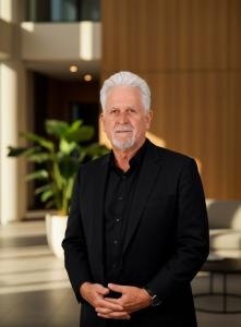 Senior male executive in a black suit standing in a modern, light-filled corporate lobby with wood paneling and indoor plants, conveying leadership, professionalism, and quantitative finance expertise.