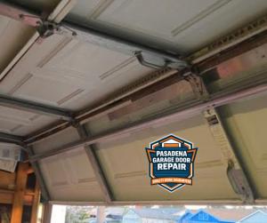 Interior view of a sectional garage door featuring metal hinges, tracks, and a center support bar, branded with the Pasadena Garage Door Repair "Quality Work Guaranteed" logo.