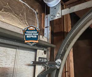 Interior view of a sectional garage door featuring metal hinges and tracks, branded with the Pasadena Garage Door Repair "Quality Work Guaranteed" logo.