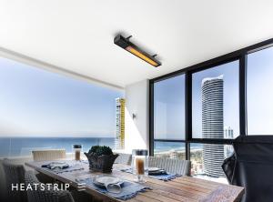 HEATSTRIP Intense electric heater installed above an outdoor dining table on a covered balcony with an ocean view.