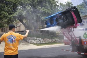 Technician cleaning a residential trash can using high-pressure water as part of a curbside waste container sanitation service in San Antonio, Texas.