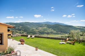 Wide view from CasaBada in Chianti Rufina, Tuscany, with a stone terrace, green lawn, loungers, and rolling hills under a blue sky