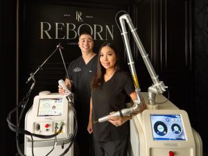 Two clinic staff members in black scrubs stand between professional laser treatment machines, holding laser handpieces, with a black wall behind them displaying the ‘Reborn Laser’ logo.