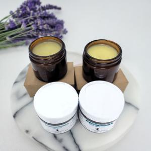 two open jars of salve sitting in front of two closed jars with a sprig of lavender flower nearby