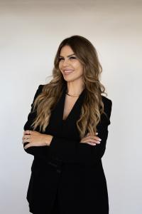 Christy Sepulveda stands with arms crossed in a black blazer, smiling in a studio portrait against a white background.