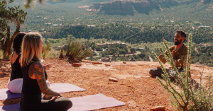 Saha Yoga leading a guided meditation for two participants seated on yoga mats overlooking Sedona’s red rock landscape.