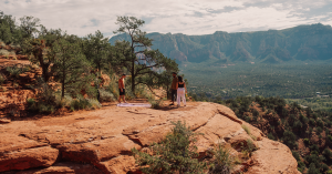 Small group practicing outdoor yoga on a red rock ledge in Sedona with sweeping views of mountains and forest below.