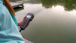 Woman holds dissolved oxygen meter in her hand while observing low dissolved oxygen in pond with a fish kill.