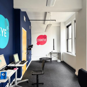 Bright exercise room featuring blue and pink walls with "Cognitive" and "Eye" decals, a trampoline, and desks with computers.