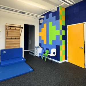 Bright and colorful playroom featuring climbing equipment, a padded mat, and chairs against a vibrant geometric wall.