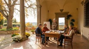 A group of adults sits at a table in the portico of an ancient Tuscan villa.