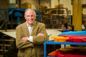 A man standing in a factory next to parts of brightly colored toys.