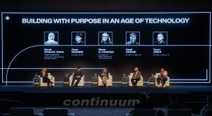 Panel discussion on stage with five speakers seated in chairs, large screen above showing "Building with Purpose in an Age of Technology" and panelist photos.