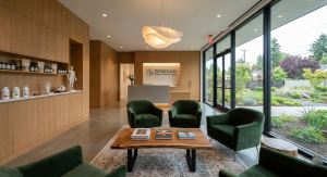 A wide-angle shot of a high-end, modern acupuncture clinic's empty waiting room. On the right, a sleek dark wood reception desk features a glass plaque with the words "Acupuncture Clinic." To the left, minimalist white leather armchairs are arranged near 