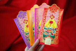Four colorway variations of CNY 2026 red packets pink, purple, orange, and red showing die-cut orchid crown and Peranakan heritage design elements