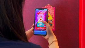 Person scanning QR code on CNY 2026 Red Packet Singapore with smartphone, demonstrating augmented reality feature that brings Singapore design elements to life on screen