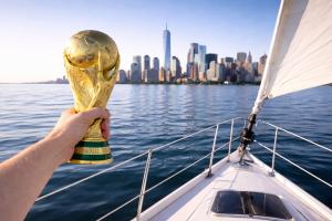 Hand holding world cup 2026 trophy on sailboat with NYC skyline in background.