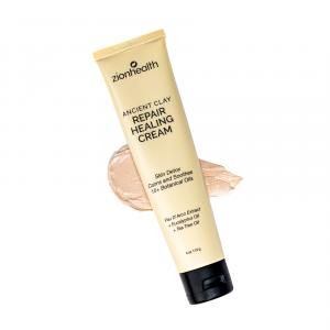 A tube of Zion Health Ancient Clay Repair Healing Cream angled over a smudge of the tan-colored mineral clay cream on a white background.