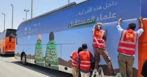 Technical staff installing a blue vinyl wrap on the side of a large bus, demonstrating the process of vehicle branding Riyadh for transport fleets.