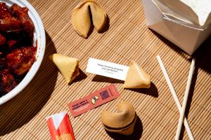 Fortune cookies on a bamboo table with chopsticks and takeaway container, showing a Beforepay branded message strip with QR code inside the cookie.