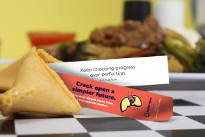 Close-up of an open fortune cookie revealing a message reading “Keep choosing progress over perfection” and a red Beforepay promotional strip.